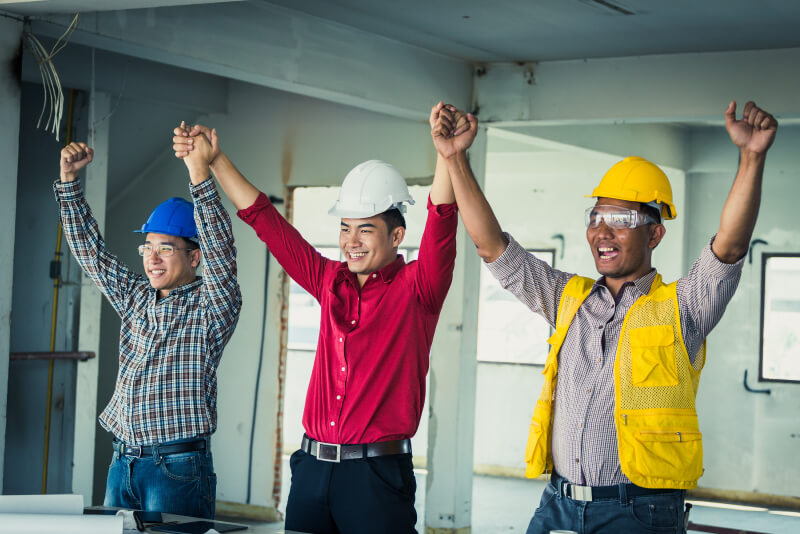 Three smiling construction workers celebrating with their arms up