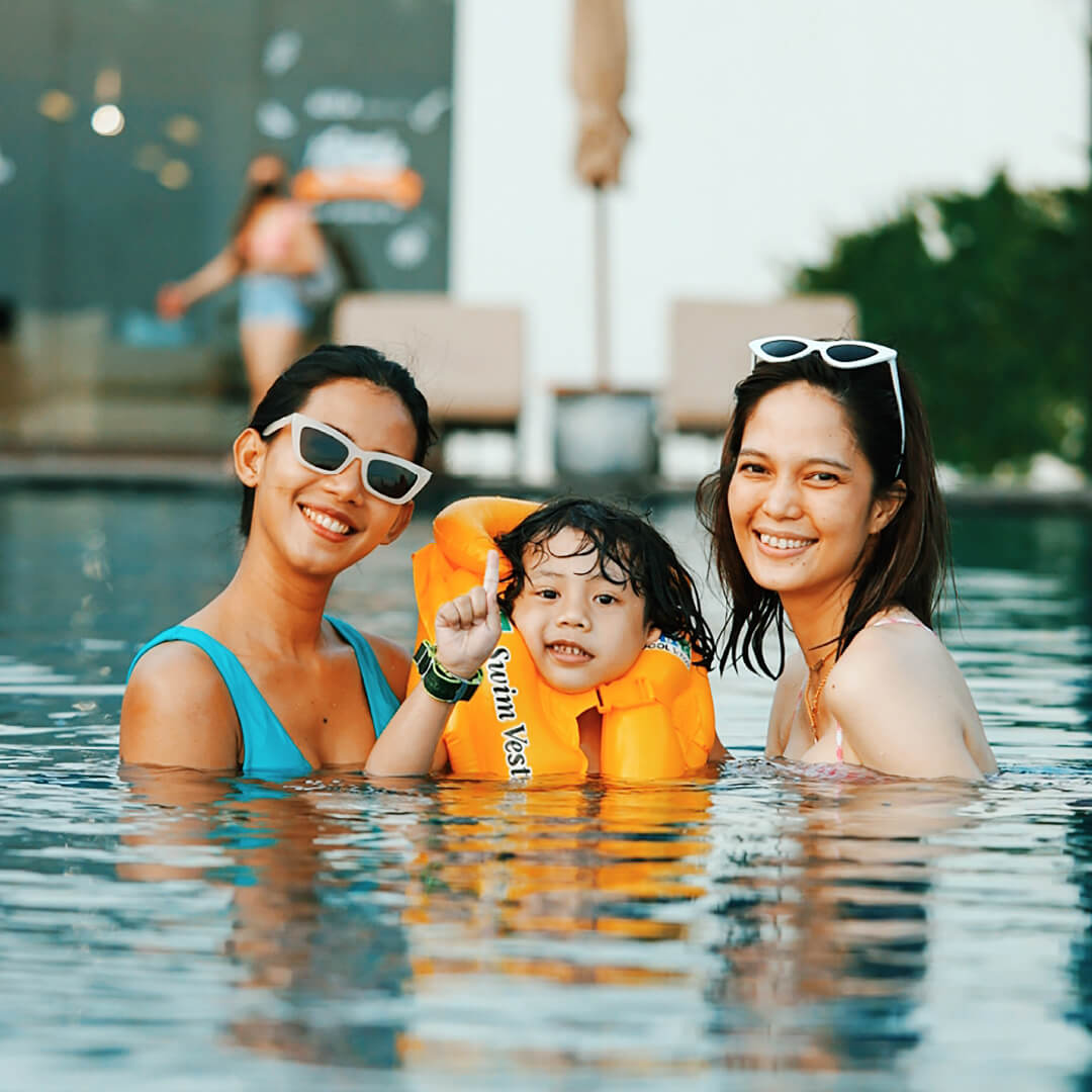 A family in the water smiling with a child in the middle with an orange life jacket