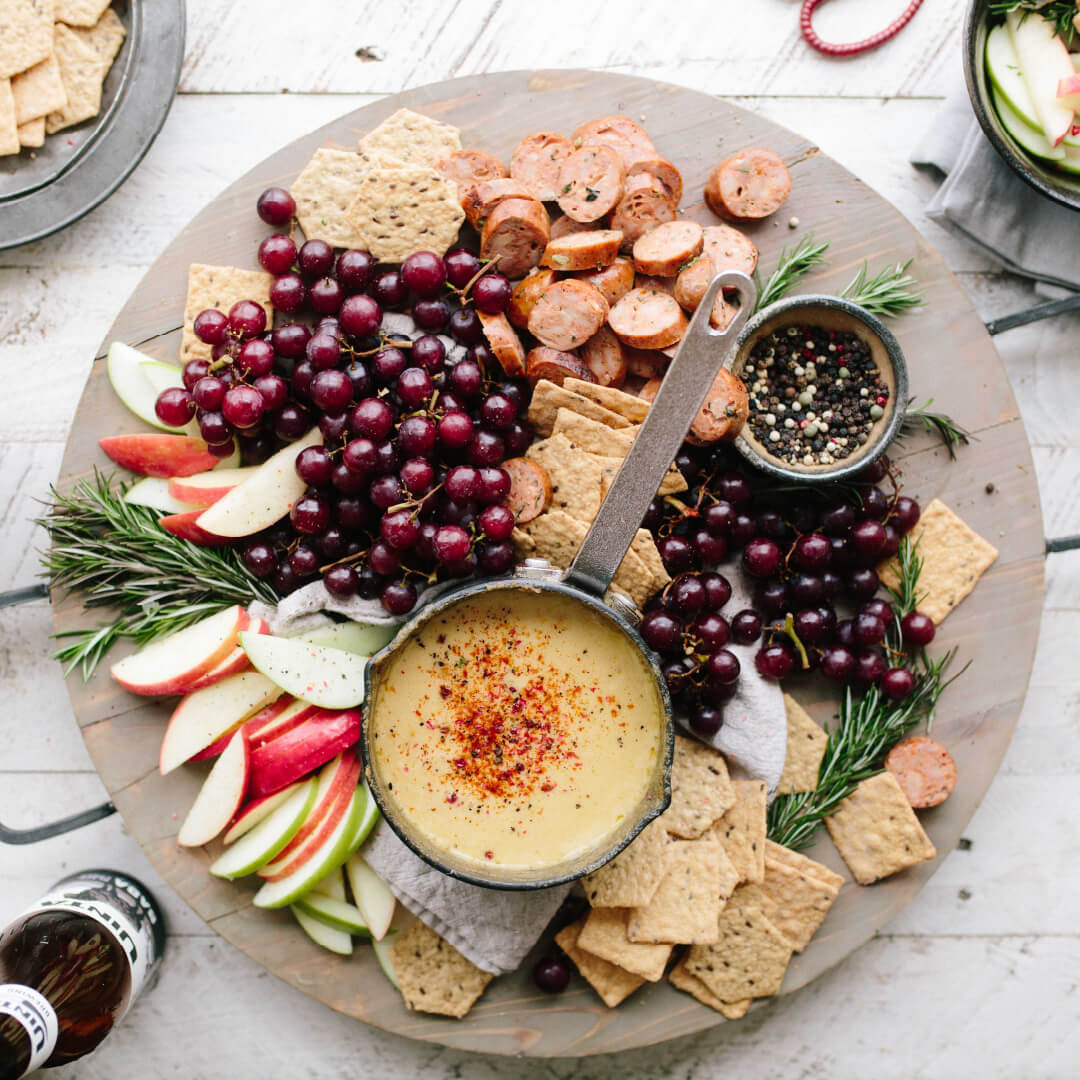 A plate of delicious snacking food, such as crackers, grapes, apples, dip, and a wine beverage