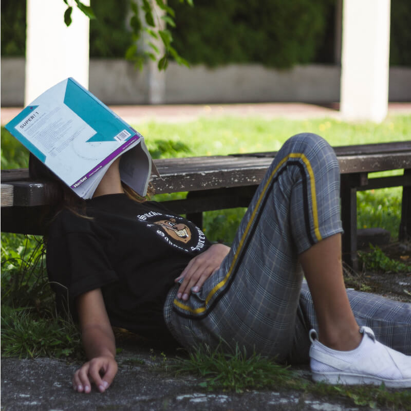 A person laying down with a book over their head due to boredom 