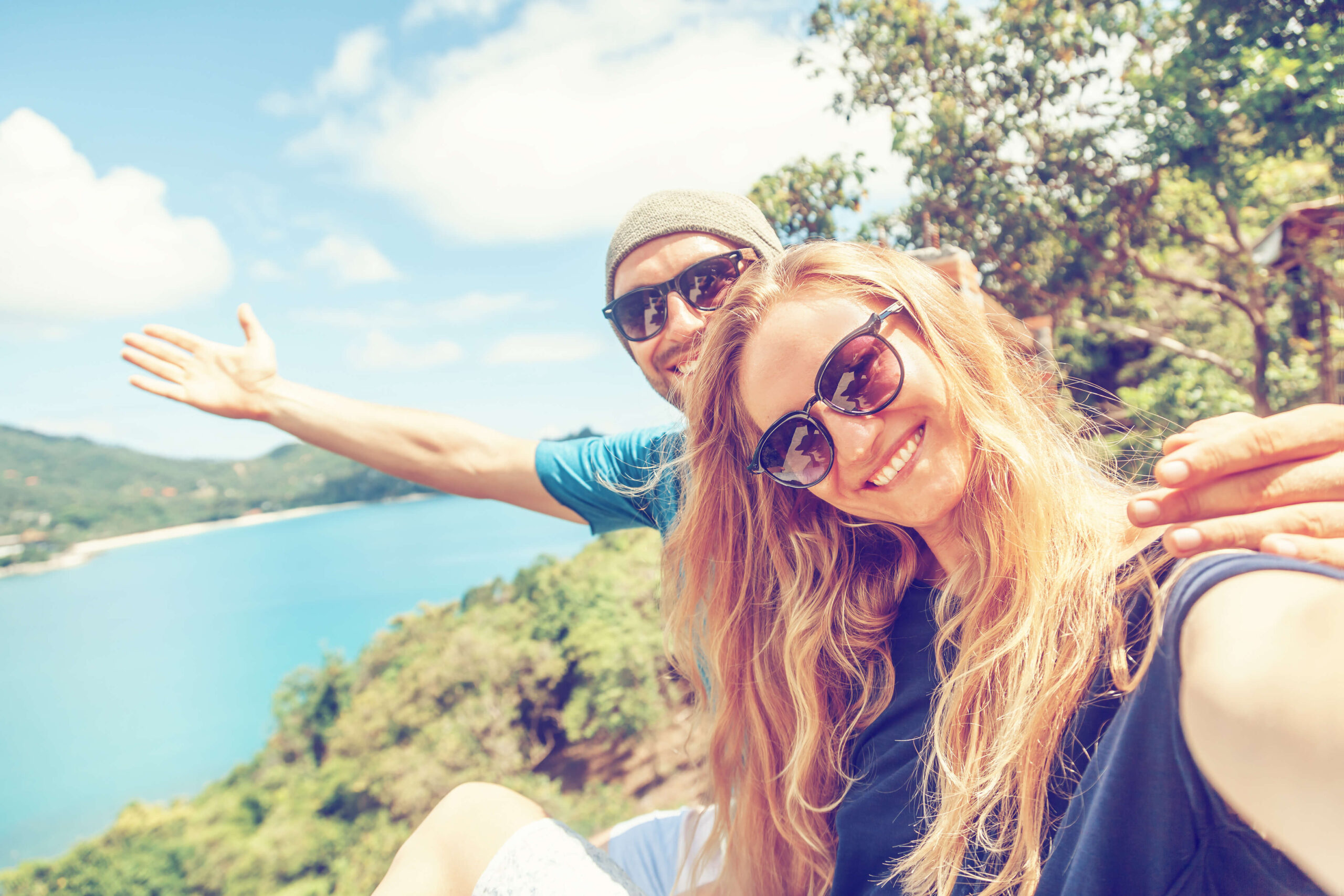 A happy, smiling couple sharing their adventure outdoors with the camera with the male gesturing to nature